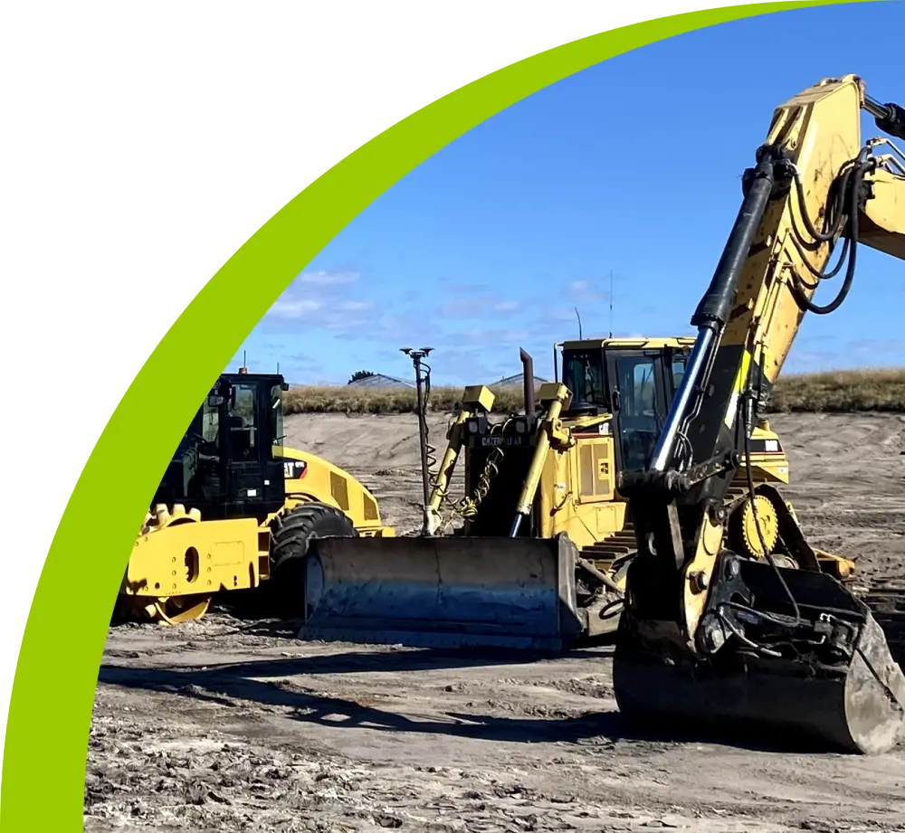 Yellow construction machinery, including bulldozers and excavators, operating on a dirt construction site under a clear blue sky. A green arc partially frames the upper left corner.